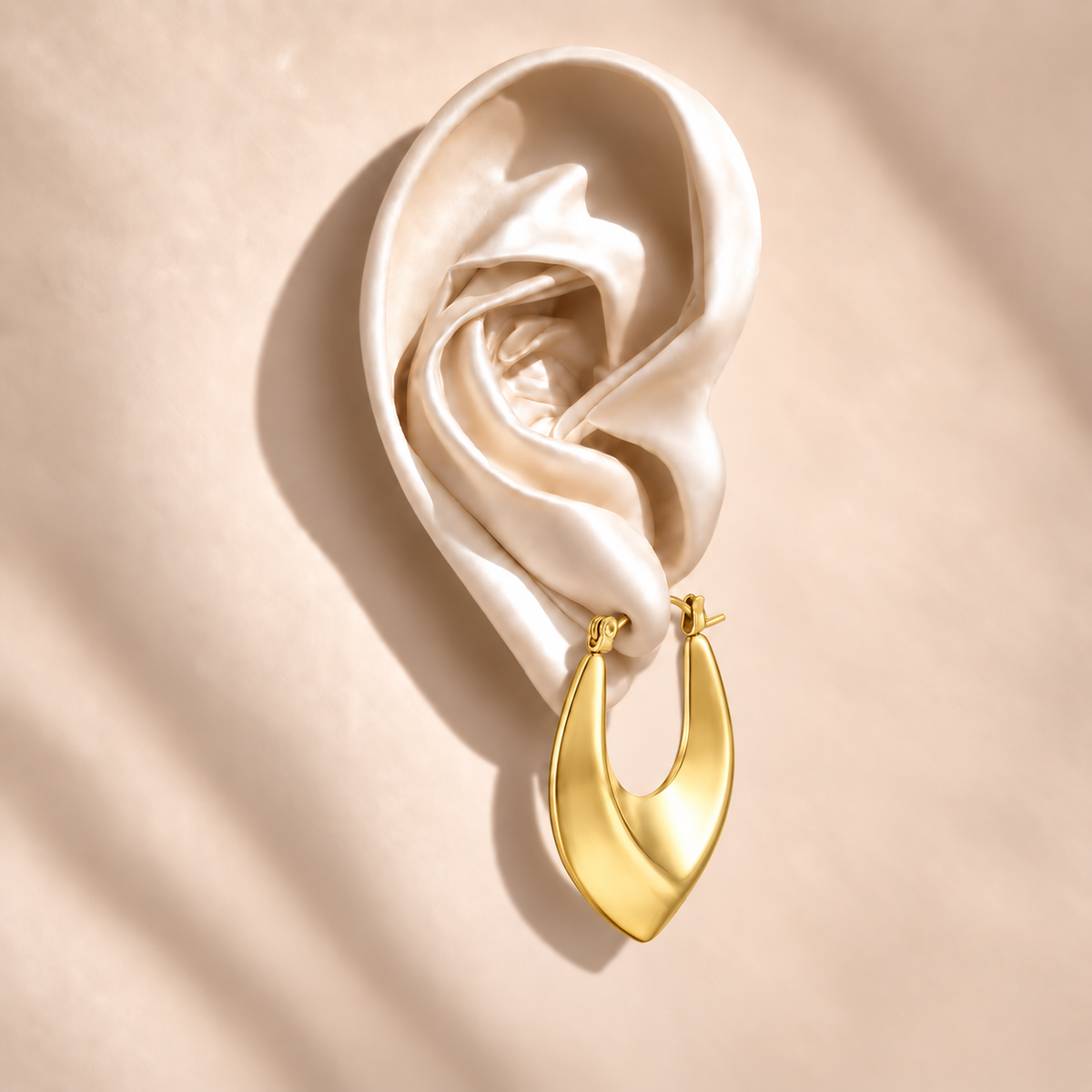Vela Gold Sculptural Hoop on an ivory satin ear