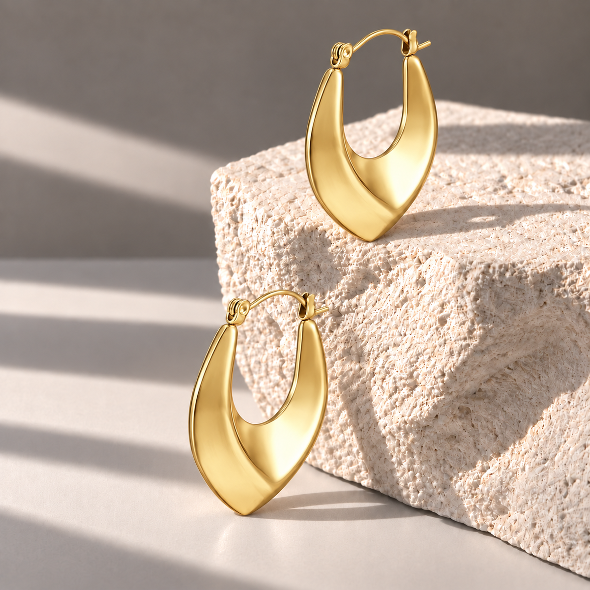 Vela Gold Sculptural Hoops on pale limestone